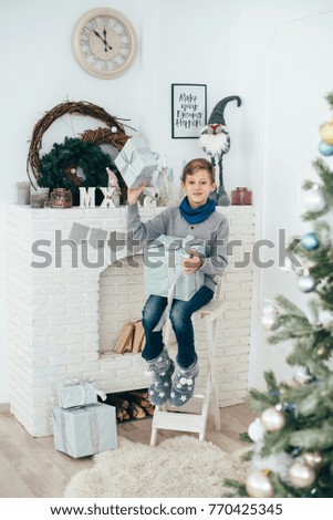The guy schoolboy sits at the fireplace and holds the box with a gift in his hands