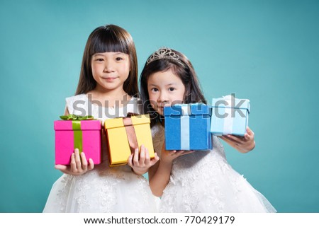 Portrait of two little asian girls holding birthday presents ,  isolated on light blue background .