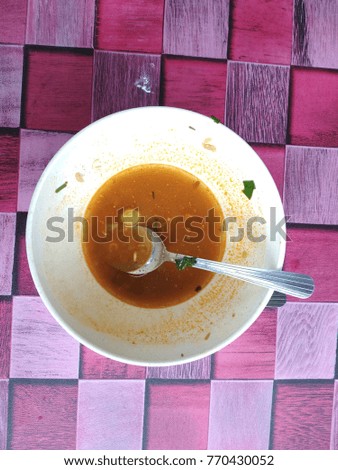 A bowl and spoon with remaining thai soup after eating isolated by square background 