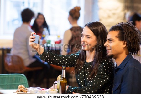 leisure, people and technology concept - happy couple taking selfie by smartphone at restaurant or bar