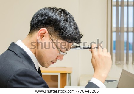 Asian businessman get headache and serious on decision in his management career on the table full of sheets, data and labtop.