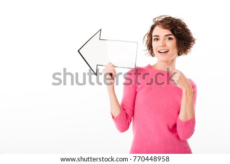 Portrait of a happy pretty girl pointing away with a paper arrow isolated over white background