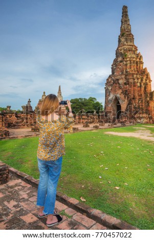 Rear view of young asian girl taking smartphone photo with mobile phone at Wat Chaiwatthanaram temple in Ayutthaya.