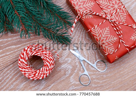 a Christmas gift tied with a red ribbon, scissors and a spruce branch on a wooden table