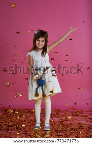 Little girl in a white dress on a pink background with a gold confetti