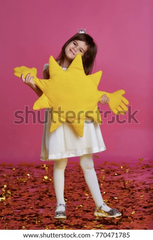 Little girl in a white dress on a pink background with a gold confetti and toy