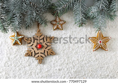 on a white snowy background lies a Christmas homemade gingerbread cookies a snowflake made of wood, a ornament,  and spruce branches. Color photo