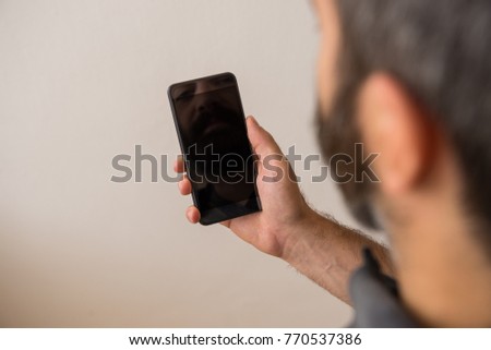 Young adult man hand holding black screen reflection smartphone on green screen background.