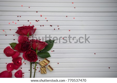 Romantic occasion photography image with fresh red rose flowers and gold color topped chocolate biscuits on natural white wood background sprinkled with small red heart shapes for any season