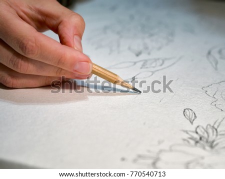 Woman's hand holding a pencil and drawing a flowers on watercolor paper. Closeup View. Shallow Depth Of Field.