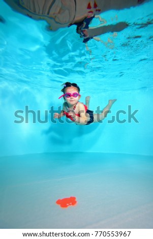 Child underwater dives to the bottom of the pool after a toy on a blue background. Portrait. Shooting under water. Vertical orientation