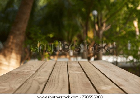 Empty top of natural wooden table for product placement and display in open shade. Coconut palm trees and green tropical plants on background. Maldives