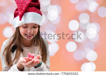 Little girl with Santa hat look at small gift box and smile.