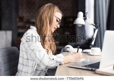 concentrated young woman writing in notebook at workplace