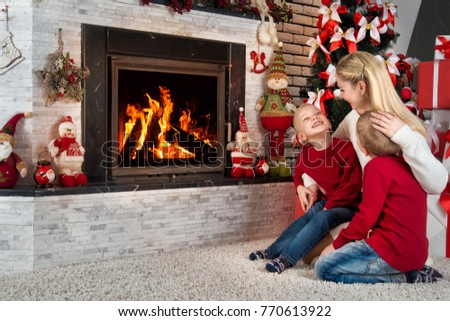 Merry Christmas and Happy Holidays!Mom and two little sons sit and relax under a Christmas tree by the fireplace.