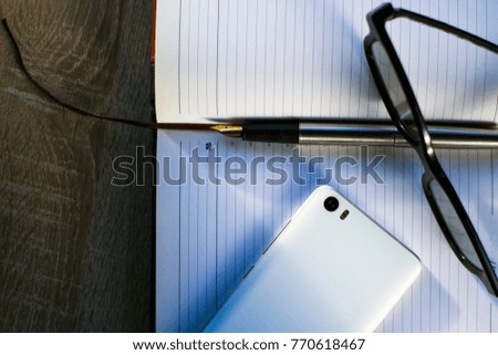 fountain pen, smartphone and glasses lie on a notebook