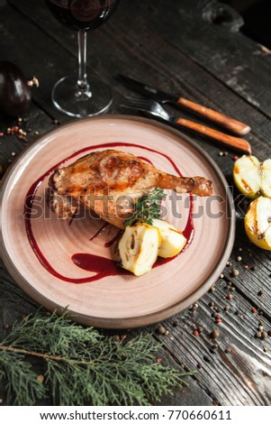 beautiful serving duck leg confit with apples and berry sauce on a wooden plate with a glass of red wine