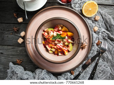 fruit salad with sauce in a ceramic plate with a cup of tea on a wooden background