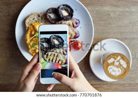 Hand with smartphone taking picture of food and coffee on wooden background                               