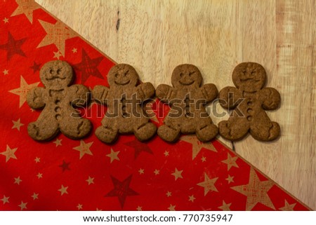 Tasty sweet gingerbread man on a wooden board and a red Christmas golden stars table cover. Typical winter holiday snack in the Western world.