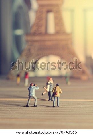 miniature people photographer taking picture of couple in paris with eiffel tower in background.