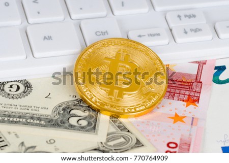 golden bitcoin metallic coin and white keyboard over dollar and euro banknotes
