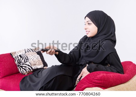 Arab beautiful woman sitting on sofa at home using remote control with white background