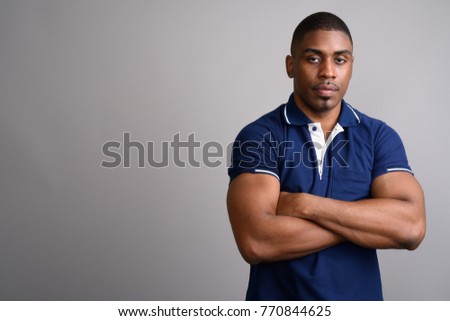 Studio shot of young handsome African man wearing blue polo shirt against gray background