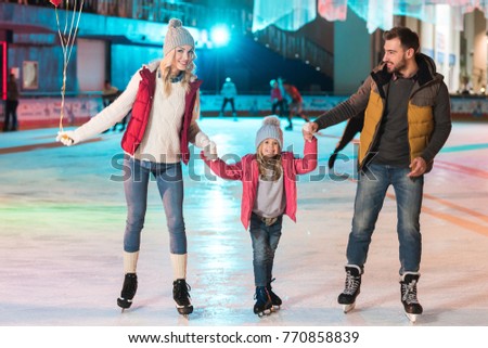 happy young family holding hands and smiling at camera on skating rink
