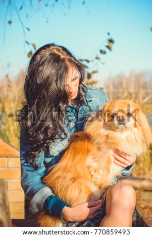 Senior dog owner girl play with pet in park outdoor, brunette girl kiss little puppy.Domestic canine pekingese.Young woman cuddling her doggy. Dog lover play with happy her dog in park