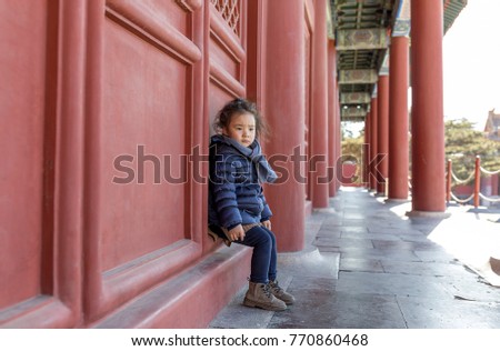 A little asian girl playing in front of the red door of a Chinese ancient building