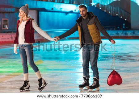 young couple holding hands while man holding heart shaped balloon on rink