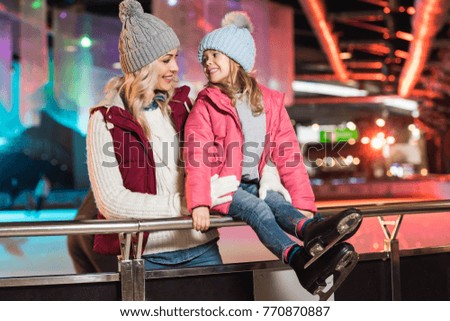 beautiful happy mother and daughter smiling each other on skating rink