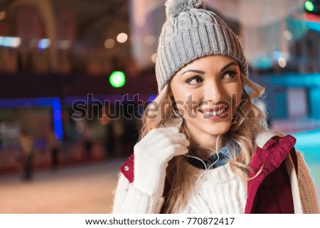 cheerful young woman in earphones looking away while ice skating on rink