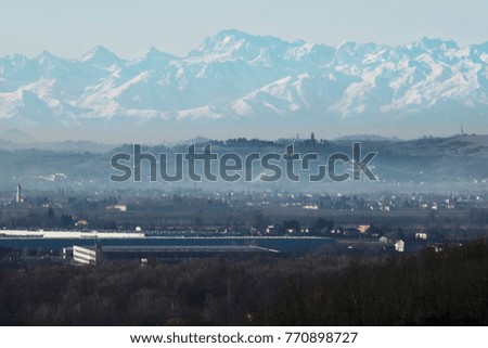 a panoramic view on hills trough fog with a big alpine range on background with snowy mountains
