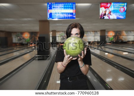 Portrait of a beautiful young girl with a bowling ball in the hands of the background of the tracks. Rest on the game at the bowling club.