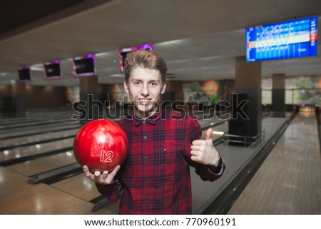 Young man likes playing bowling. Young handsome man standing with a bowling ball in his hands and showing his thumb up.