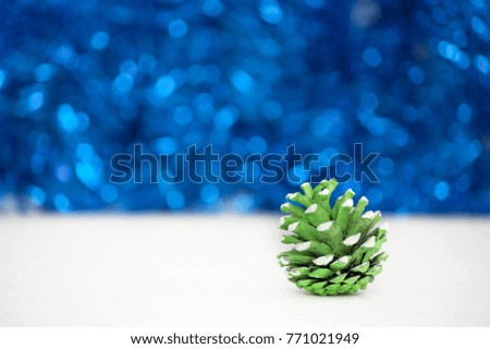 Winter Christmas decoration. Cute natural pine cone, painted in green and white color, blue bokeh texture and white background. Shallow depth of focus. Copy space for text.