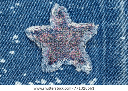 Ripped denim star patch with glittering sequins on denim  fabric background with white bleached spots. Denim jeans fashion background.