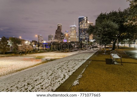 Empty bench and Downtown Houston at  night with big and fluffy snowflakes fell on meadow grass at Eleanor Park. Snow is extremely rarely happen here, it has only fallen in Houston 35 times since 1895