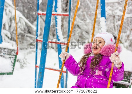 Little kid girl swinging on the winter park.