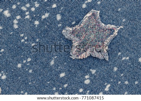 Ripped denim star patch with glittering sequins on denim  fabric background with white bleached spots. Denim jeans fashion background.