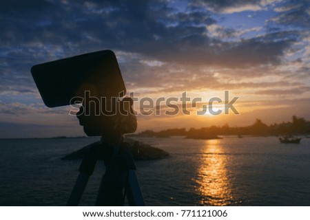 sunset or sunrise photographer by smart phone. silhouette of smart phone shooting a sunset or sunrise moment at the sea outdoors with beautiful light and cloud. travel concept. 