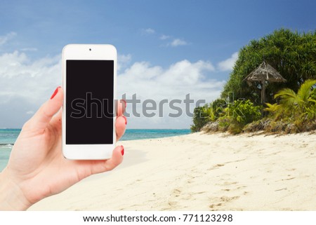 womans  hand holds a mobile phone at  beautiful beach on a caribbean sea in summer time