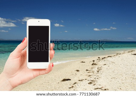  female hand holds a mobile phone at a beautiful beach on a caribbean in summer time