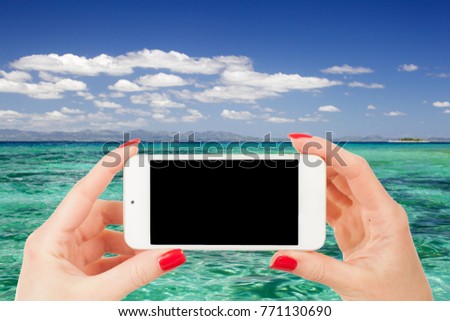 female hand holds a mobile phone at a beautiful beach on a caribbean in summer time