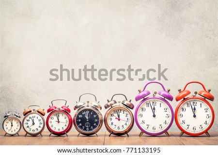 Seven retro alarm clocks with last minutes to twelve o'clock on wooden table front concrete wall background. Vintage old style filtered photo