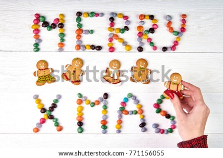 Beautiful Christmas inscription of sweet dragees, gingerbread, a female hand taking Christmas cookies. New Year's photo with a female hand in a knitted sweater with a red manicure.