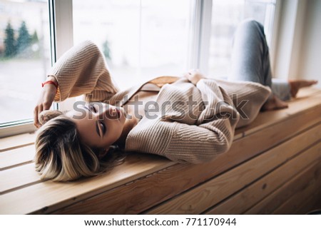 Beautiful white stylish woman in cozy scandinavian interrior sits at home near the big window 