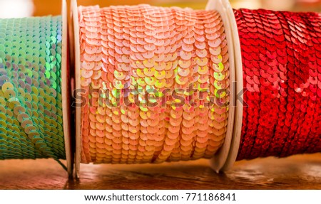 Cose up of shiny rolls of colorful sequins tape, multi-colored over a wooden table in a blurred background